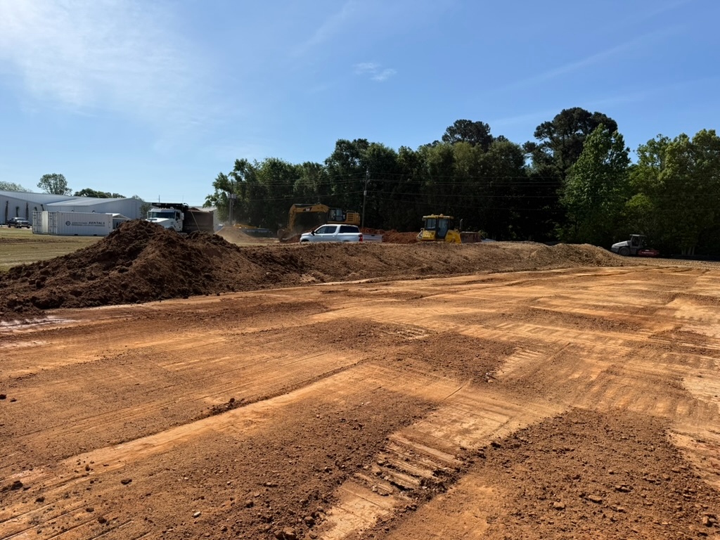 Wide graded dirt building pad with rubber-tire excavator, prepared and ready for the next trade