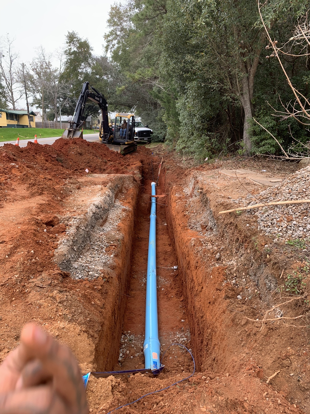 Blue water main pipe installed in an open trench with an excavator nearby